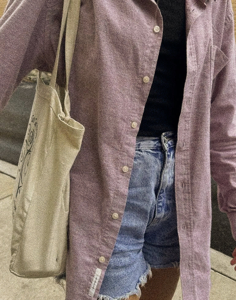 Close up of a dusty mauve button up worn open over a black top and light denim, with a canvas tote.