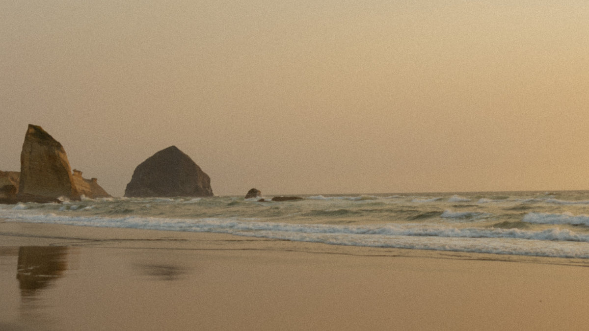 Sea stack off an Oregon beach at dusk, warm haze hanging over the water.