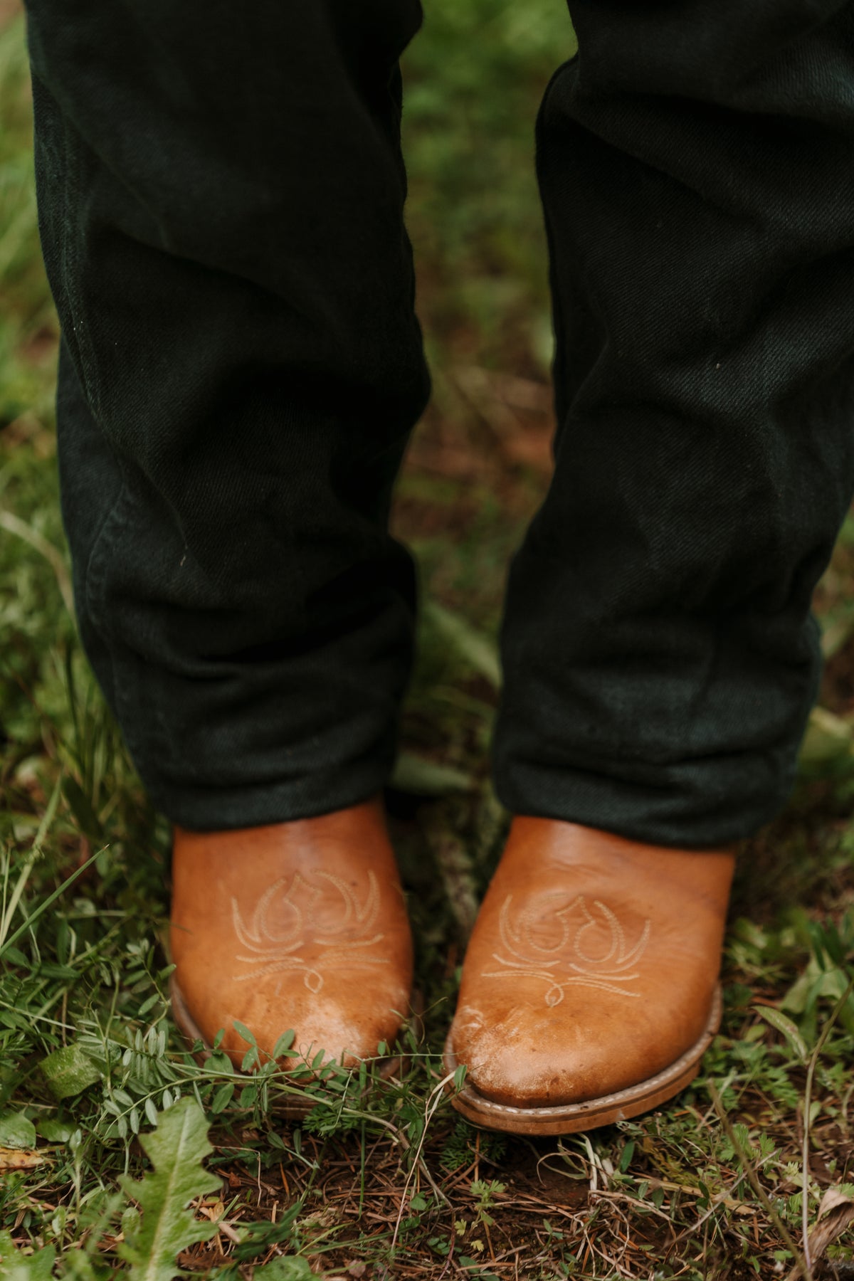Caramel cowboy boots worn with black jeans, standing in green grass.