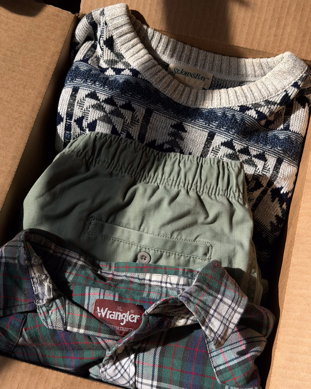 Navy and cream patterned knit sweater folded over sage green trousers inside a Forager's Goods box