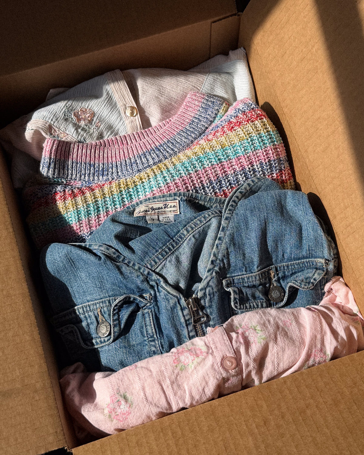 Packed box: rainbow striped knit, denim jacket, cream embroidered top and a soft pink floral piece.