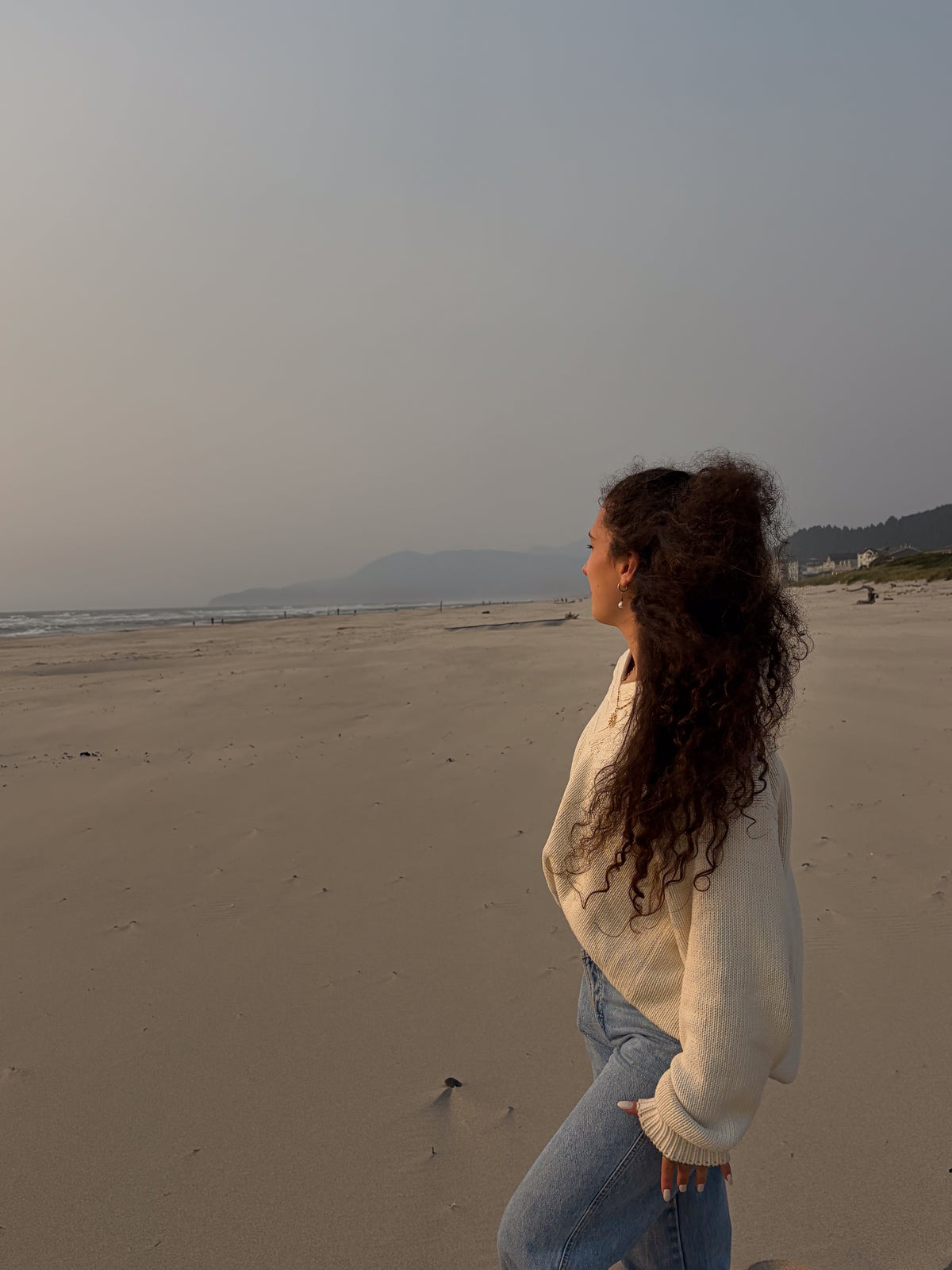 Oatmeal knit sweater and jeans on a wide empty beach in hazy evening light.